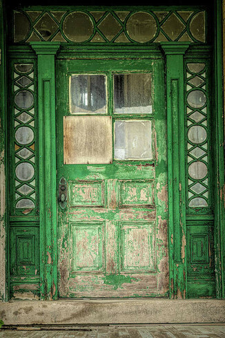 A green door with beautiful details on the  glass surrounding the door.  The peeling paint adds to the textures of the door.  This door is from an empty abandoned  Bachelor's Officer quarters at Fort Hancock on Sandy Hook.